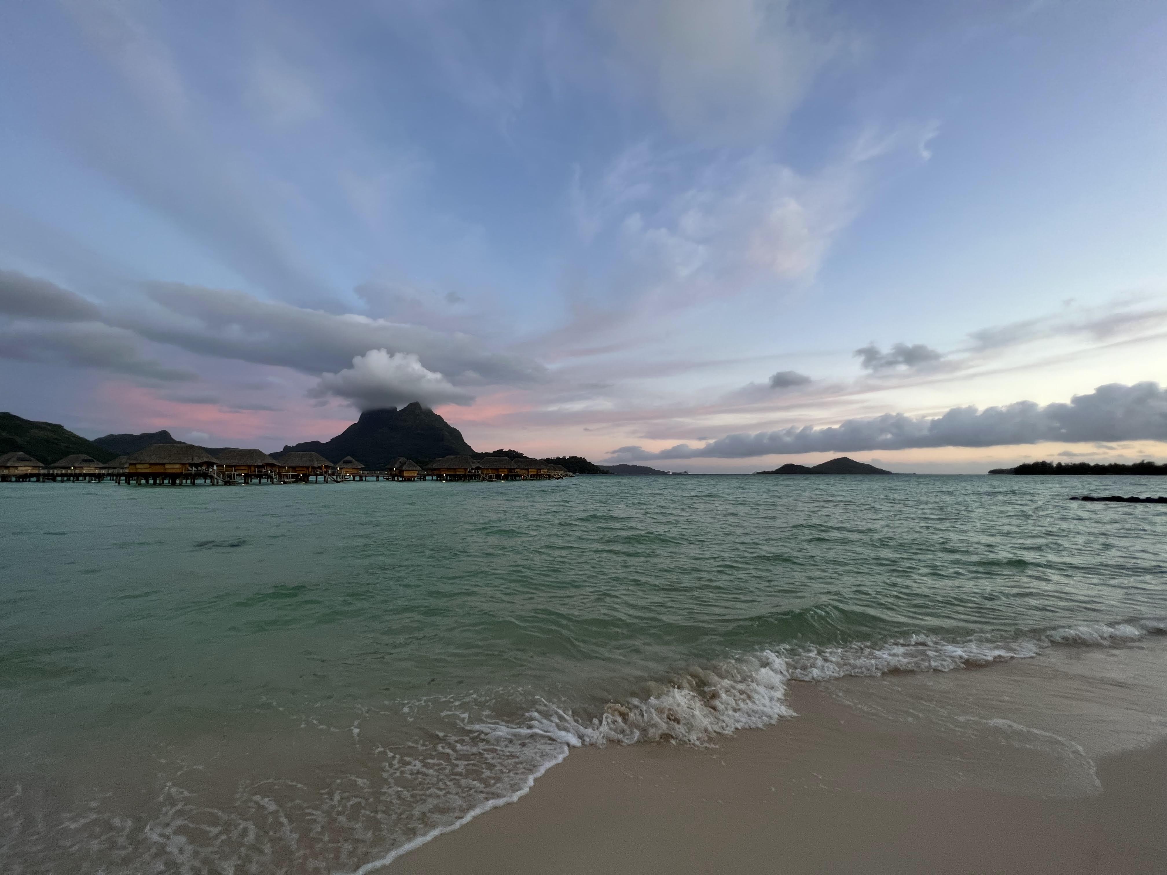 Tropical paradise with overwater bungalows Tropical paradise with overwater bungalows on a pristine beach, turquoise ocean waters, and lush green mountains in the background during golden hour